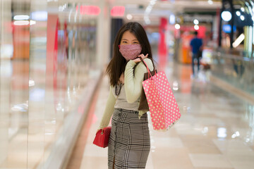 happy Asian at shopping mall in new normal lifestyle - young attractive and beautiful Korean woman with face mask holding shopping bags at fashion center excited enjoying sales