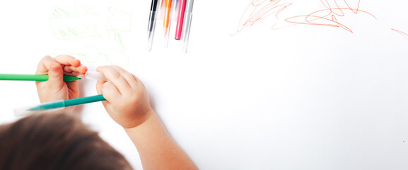 Little child draws on white paper with colored felt-tip pens, teaching children to draw