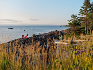 Two red chairs on a rocky coastine at sunrise in Petit-Rocher, New-Brunswick