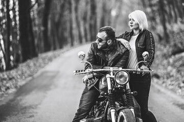 Naklejka premium Pretty couple near motorcycle on the road in the forest with blured background