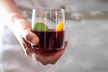 Female hand holding glass with sangria drink or punch making with red wine and fruit.
