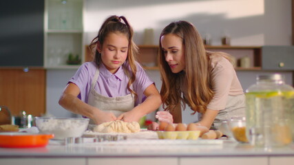Obraz na płótnie Canvas Attractive woman teaching girl to prepare dough for cookies on modern kitchen