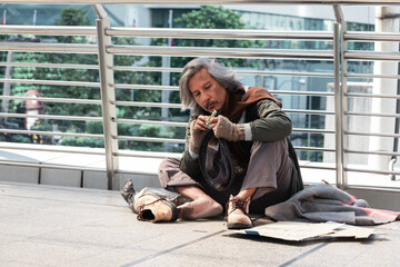 Homeless man is sitting down on walkway in town.