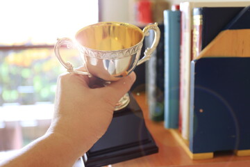 Close-up of a hand holding an ancient trophy Stacks of books in the background selective focus and shallow depth of field