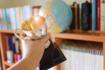 Close-up of a hand holding an ancient trophy Stacks of books and globes in the background selective focus and shallow depth of field