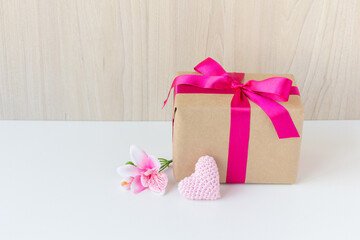 Happy Women's Day, Happy Mother's Day, Happy Valentine's Day and Happy Birthday. Have a flower, a crochet heart, a beautiful gift wrapped in a pink ribbon. Wooden background. White base. Copy space.