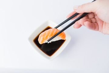 Female dipping tasty salmon nigiri with chopsticks into bowl with soy sauce on white background. Space for copy.