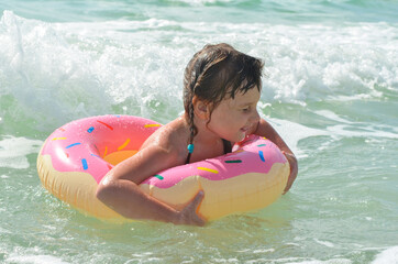 A little girl in a swimming circle is swimming in the sea. The child has fun on vacation. Sea foam and wave splashes