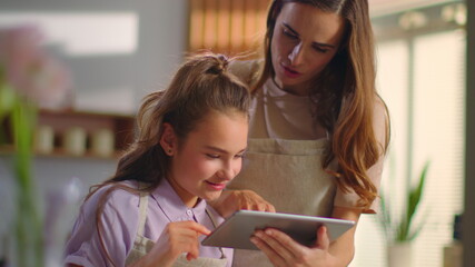 Smiling woman and girl looking for recipe on pad at kitchen in slow motion