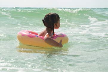 A little girl in a swimming circle is swimming in the sea. The child has fun on vacation. Sea foam and wave splashes