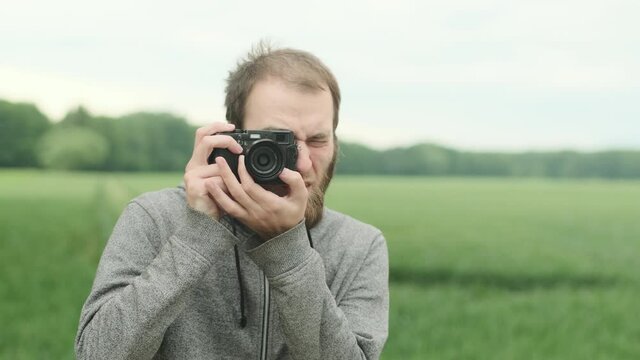 European hipster man taking photo with film camera, nature around.
