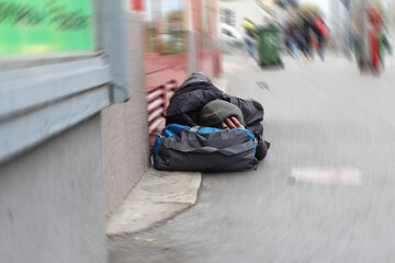 Homeless person sleeping on the street in front of a shop in a big city