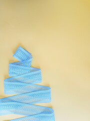 Cotton openwork blue ribbon folded in the form of a Christmas tree on a yellow background.