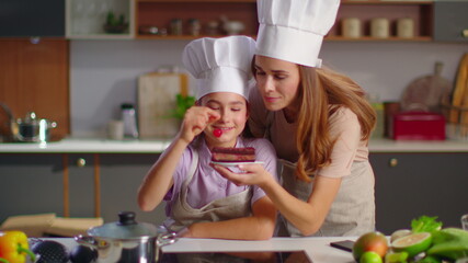 Confectioner and mother putting cherry on cake at kitchen in slow motion