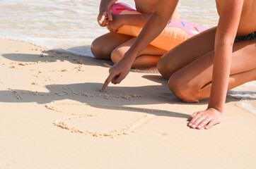 Happy children on vacation on a sandy beach. Brother and sister draw with their finger in the sand. Concept summer lifestyle