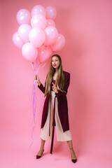 stylish young girl in burgundy clothes and pink balloons on a pink background
