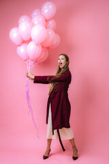 stylish joyful young girl in burgundy clothes and pink balloons on a pink background