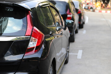 Closeup of rear, back side of black car with  other cars parking in outdoor parking area in sunny day.