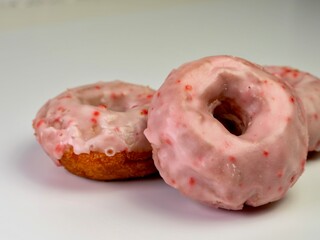 Cherry doughnut / donut with pink cherry glaze on top piled up on a white counter. Delicious baked goods.