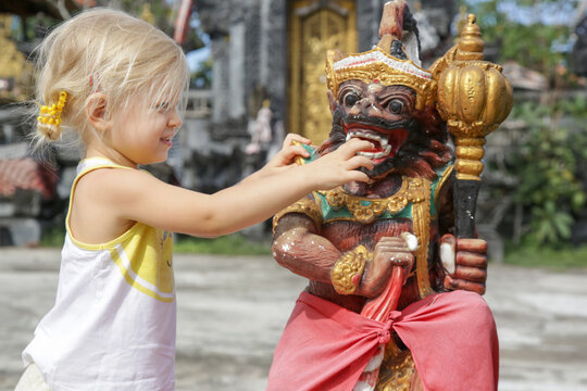 Adorable Caucasian Toddler Girl Playing In Front Of Hindu Temple. Child Playing With Traditional Colorful Barong Statue.