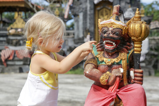 Adorable Caucasian Toddler Girl Playing In Front Of Hindu Temple. Child Playing With Traditional Colorful Barong Statue.