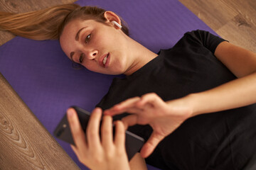 Young woman lying on yoga mat on mobile phone
