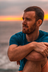 Summer lifestyle, a young dark-haired Caucasian man in a blue shirt on a sunset by the sea. Pensive looking left