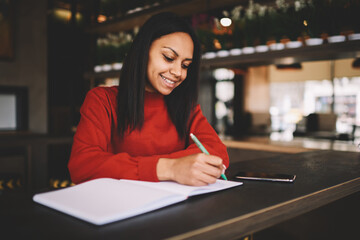 Successful young dark skinned manager planning new marketing project making note in coffee shop