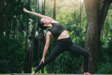 Fototapeta premium Asian woman practicing yoga in Warrior Pose (Virabhadrasana) on the mat in outdoor park.