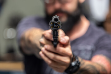 Shallow depth of focus action portrait of serious and attractive hitman or special agent man holding gun pointing the handgun to the camera on dark background.