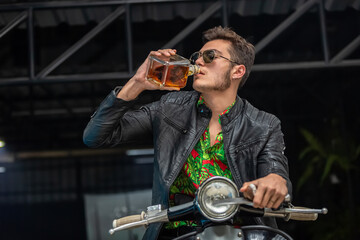 Sporty biker handsome rider male drinking whiskey from bottle.