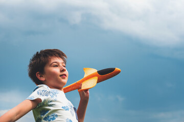 Close-up happy kid playing with toy airplane against stormy summer sky.