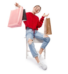 Young beautiful smiling girl in red sweetshot and blue jeans with paper bags for shopping sitting...