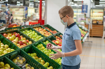 Teenager in the supermarket wearing a mask and gloves. He chooses fruit.