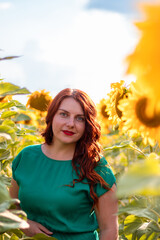Beautiful young girl with long hair in a green summer dress in a sunflower field at sunset day
