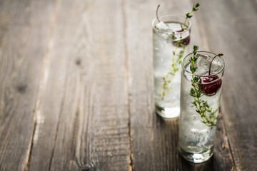 Gin based cocktail with cherries and thyme herbs on the rustic background. Selective focus. Shallow depth of field. 