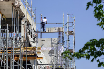 Konzept Sicherheit auf einer Baustelle: Ein großes Gebäude ist komplett entkernt und eingerüstet für die Sanierung, mit einem ungesicherten Arbeiter und viel blauem Himmel – sehr viel Copyspace, selek