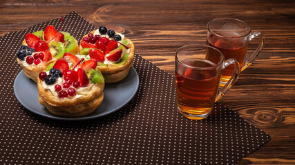 Home made cake with cream and fruit and hot tea on wooden table.