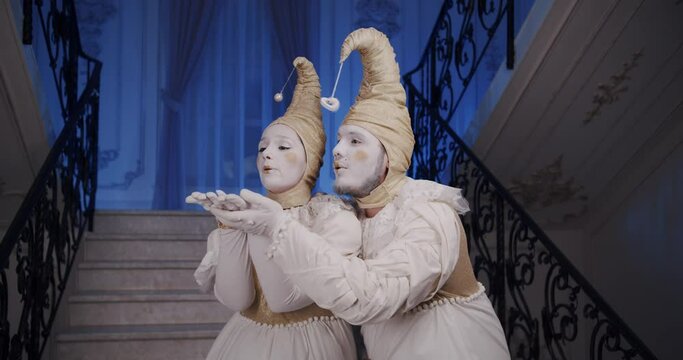 A pair of mime lovers in beautiful old theatrical costumes perform a magic performance and blow a kiss together.