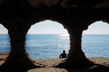 Una persona sola
 sentada al borde del mar vista desde un circulo de piedra 