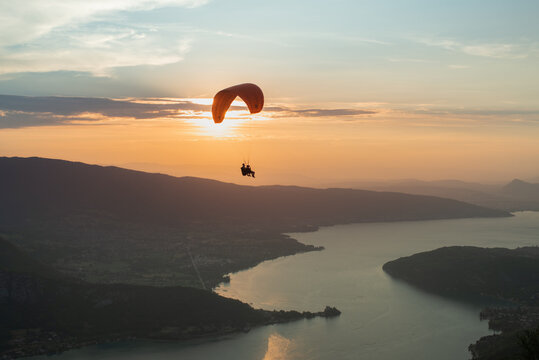 tandem paraglider flying over a beautiful winding lake at sunset.