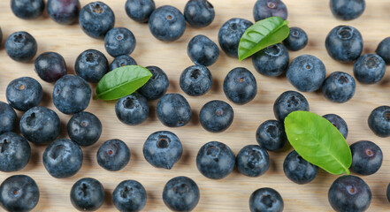   blueberry berries with green leaves on light wooden background top view 