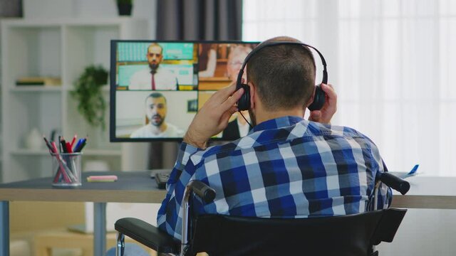 Entrepreneur immobilized in wheelchair talking with his team using headphones during a video call. Handicapped invalid paralysed freelancer, immobilized entrepreneur working from home, ilness