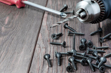 Metal screws and an electric drill on a wooden background. Tool for fixing and repairing. Copy space
