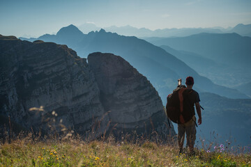 young man standing on a mountain pointing down to the valley in the distant horizon.
