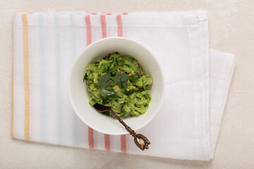 Mexican guacamole sauce in a white bowl on a concrete background, top view, close up