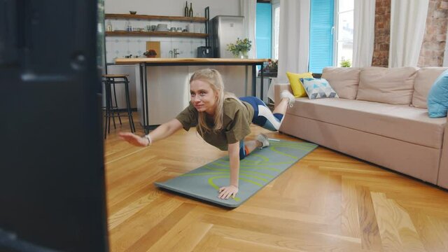 Young woman doing exercises at home watching sport video
