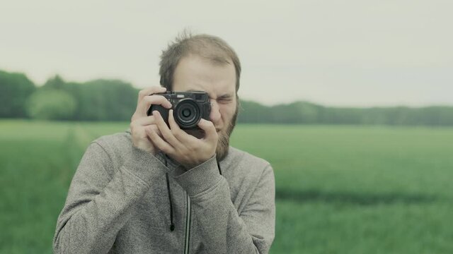 European hipster man taking photo with film camera, nature around.
