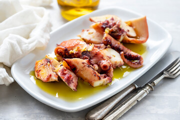 grilled octopus with olive oil on white dish on ceramic background