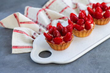 Mini strawberry tartlets on ceramic board with linen napkin on stone table